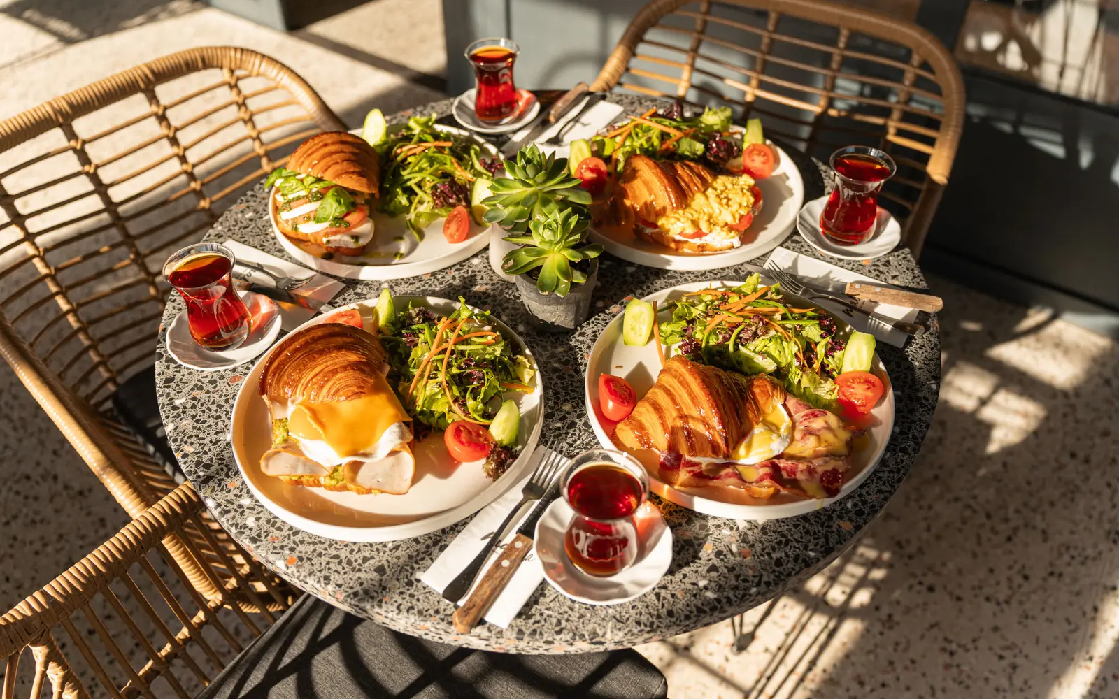 Sunlit brunch table with croissants, salads and tea