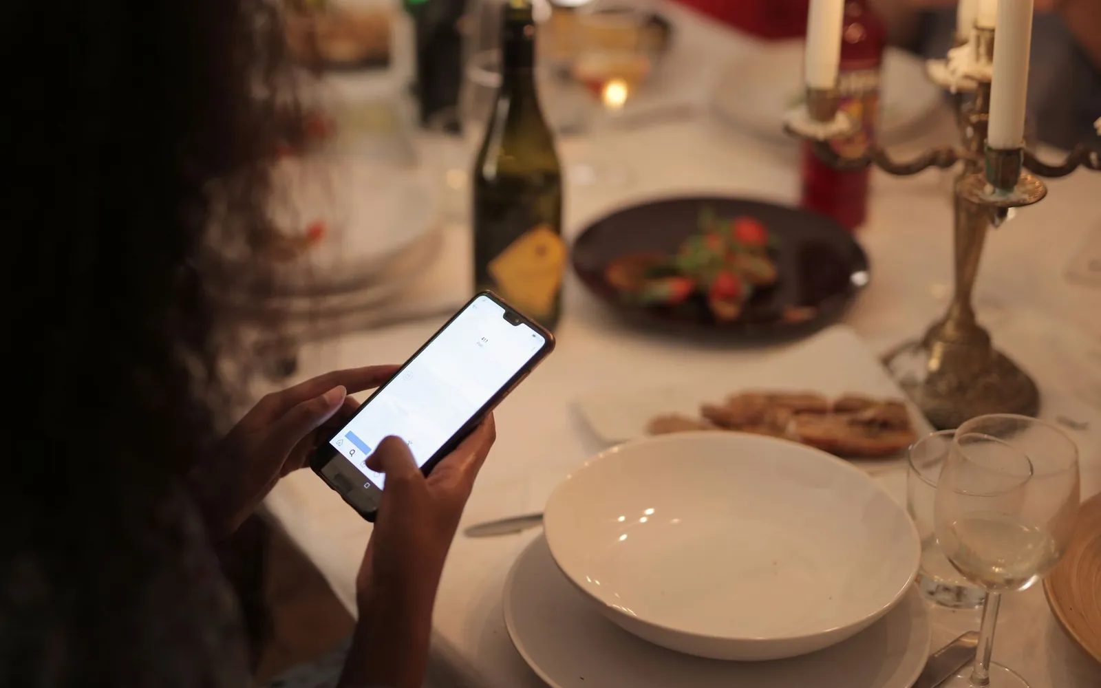 A guest checks a smartphone at a candlelit dinner table