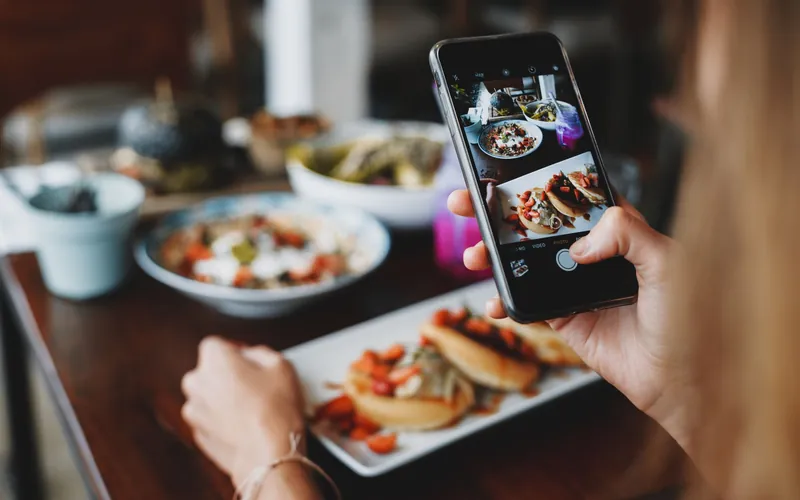 A diner photographs plates of food with a smartphone at a cafe table